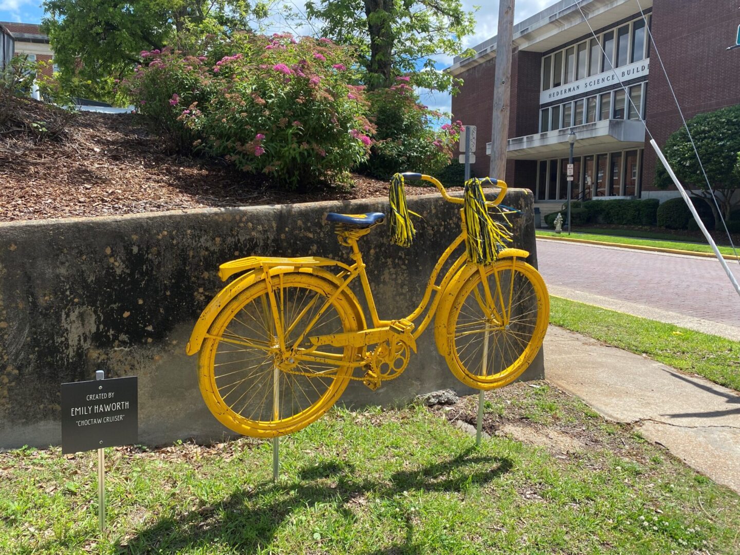 A yellow bicycle is on the grass near some bushes.