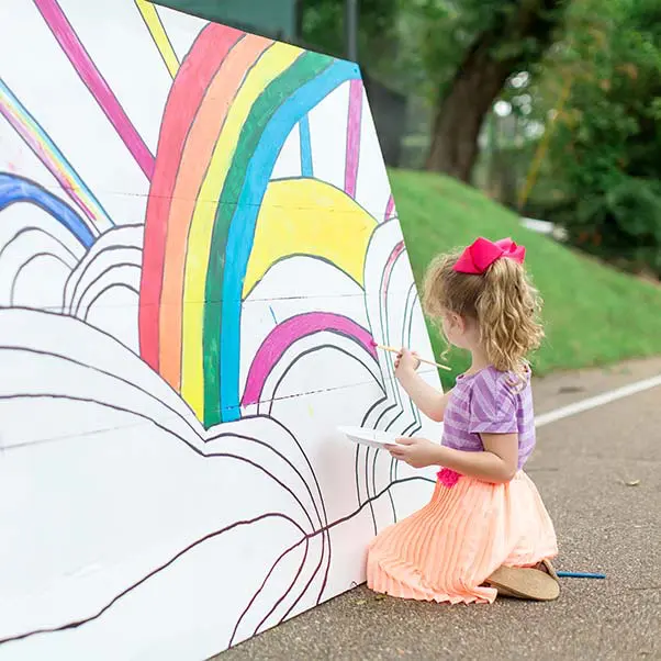 A little girl painting a rainbow on the side of a wall.